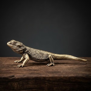 Op de afbeelding: Gedetailleerd messing beeldje van een baardagame. Het reptiel staat op een houten oppervlak, met een donkere achtergrond. De schubben en kenmerken van de hagedis zijn ingewikkeld gedetailleerd en tonen een realistisch ontwerp.