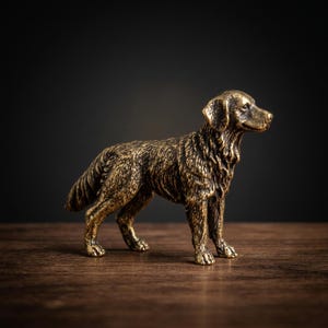 May include: A bronze-colored dog figurine in a standing pose. The sculpture has detailed fur texture and is set against a dark background. The dog is positioned on a wooden surface, showcasing its realistic features.