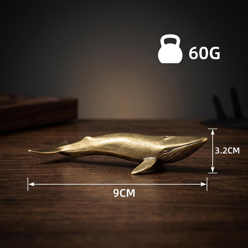 May include: A bronze whale figurine, 3.5 inches long and 1.3 inches tall, weighs 2.1 ounces. The whale is detailed with fins and a curved tail. The image includes a weight icon and the number 60G.