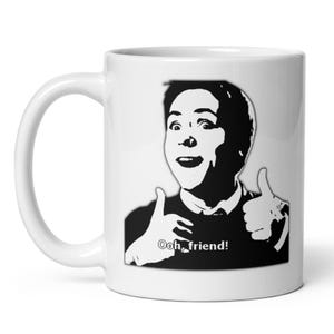 May include: White ceramic mug featuring a black and white illustration of a person giving two thumbs up. The text "Ooh, friend!" is below the thumbs. The mug has a curved handle.