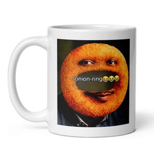 Könnte beinhalten: Weiße Keramik-Tasse mit einem humorvollen Bild eines Zwiebelrings mit Gesicht und dem Text "sonion-ring" mit weinenden Emojis. Die Tasse hat einen gebogenen Henkel und eine glänzende Oberfläche.