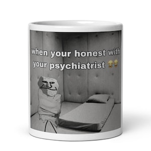 Op de afbeelding: Een witte keramische mok met een zwart-witte afbeelding van een gestoffeerde kamer met een bed en een figuur in een dwangbuis. De tekst luidt "when your honest with your psychiatrist", gevolgd door twee lachende emoji's met tranen.