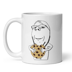 Könnte beinhalten: Weiße Keramik-Tasse mit einer Cartoon-Illustration einer Figur mit Brille, die einen Schokoladen-Chip-Keks hält. Die Tasse hat einen gebogenen Griff und eine glänzende Oberfläche, geeignet für heiße oder kalte Getränke.