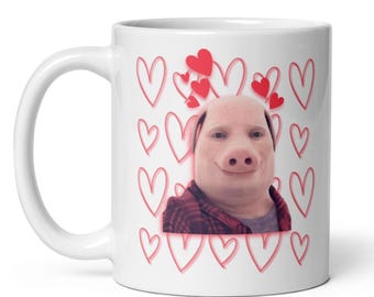Peut inclure: Mug en céramique blanche avec un visage de cochon portant une chemise à carreaux rouges, entouré de cœurs rouges et de cœurs flottants. La tasse a une poignée incurvée et une surface lisse.
