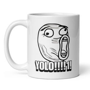 Puede incluir: Taza de cerámica blanca con una ilustración en blanco y negro de una cara de meme. La cara tiene los ojos muy abiertos y la boca abierta. Debajo de la cara está el texto "YOLO!!!!1!" en negrita negra. La taza tiene un asa curva.