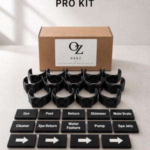 May include: A Pro Kit set featuring a brown cardboard box with an Oz Hauz label, twelve black semi-circular pipe clips, and fifteen black rectangular labels. The labels include text for Spa, Pool, Return, Skimmer, Main Drain, Cleaner, Spa Return, Water Feature, Pump, Spa Jets, and four white arrow symbols.