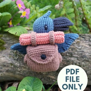 Puede incluir: Un pájaro azul tejido a ganchillo con una mochila marrón y un saco de dormir rosa. El pájaro tiene alas y pico azul oscuro. La imagen incluye el texto "PDF FILE ONLY" en un círculo blanco. El fondo es natural.