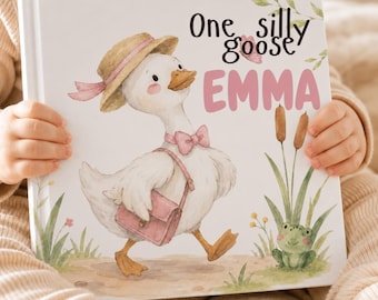 May include: A hardcover children's book with a white cover featuring a watercolor illustration of a white goose wearing a straw hat, a pink bow tie, and a pink satchel. The text reads One silly goose EMMA in black and pink lettering.