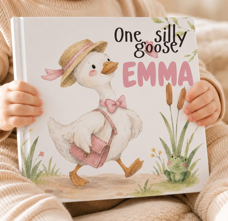 May include: A hardcover children's book with a white cover featuring a watercolor illustration of a white goose wearing a straw hat, a pink bow tie, and a pink satchel. The text reads One silly goose EMMA in black and pink lettering.