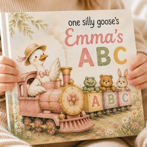 May include: A hardcover children's book titled one silly goose's Emma's ABC. The cover features a watercolor illustration of a white goose in a straw hat driving a pink steam train, followed by three train cars carrying a frog, bear, and rabbit.