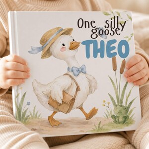 May include: A hardcover book with a white cover featuring a watercolor illustration of a white goose wearing a straw hat, a blue bow tie, and a brown satchel. The text reads One silly goose THEO. A small green frog and cattails are visible.