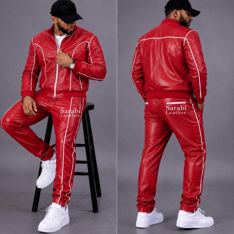 May include: A red leather tracksuit featuring a zip-up jacket and matching pants with white piping accents. The jacket has a stand-up collar and long sleeves. The pants have a straight-leg fit. The text Sarabi Leather is printed on the pants.