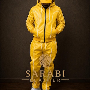 May include: Yellow leather tracksuit with white trim, including a hooded jacket, pants, and a baseball cap. The jacket has a black zipper. The brand name "SARABI LEATHER" is displayed in white text.