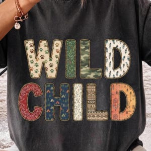 May include: A black t-shirt featuring the text WILD CHILD in large block letters. Each letter has a unique pattern, including paw prints, camouflage, leaves, feathers, paisley, camping tents, floral, geometric, and arrow designs with a stitched border.