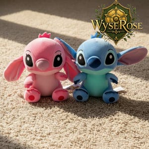 Puede incluir: Dos peluches: uno rosa con corona y otro azul con orejas grandes. Ambos tienen ojos negros grandes y est&aacute;n sentados sobre una alfombra beige. El logotipo de WyseRose est&aacute; en el fondo.