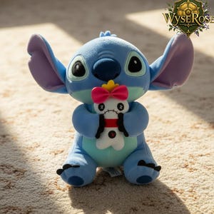 Puede incluir: Un peluche azul de un personaje de dibujos animados con orejas grandes y ojos negros, sosteniendo una mu&ntilde;eca blanca m&aacute;s peque&ntilde;a con un dise&ntilde;o rojo y negro. El peluche tiene un cuerpo azul claro, detalles en azul oscuro y orejas internas moradas.