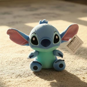 Puede incluir: Un peluche del personaje Stitch de la pel&iacute;cula de Disney Lilo & Stitch. El juguete es principalmente azul con una panza azul claro y orejas rosadas. Tiene ojos negros grandes y una peque&ntilde;a etiqueta adjunta.