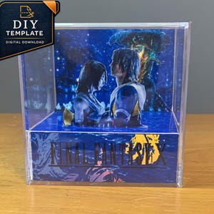 Puede incluir: Una vitrina de cubo de acrílico transparente que contiene un diorama de papel multicapa con dos figuras de pie en el agua sobre un fondo azul oscuro. El panel frontal muestra el texto FINAL FANTASY X en letras negras sobre un gráfico azul.