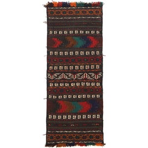 May include: A rectangular, hand-woven rug with a dark brown background and colorful geometric patterns. The rug features red, blue, green, and orange accents, with fringed edges. The design includes repeating shapes and a central pattern with a gradient of colors.