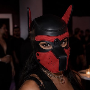 Puede incluir: Una capucha inspirada en un animal en color negro y rojo, con orejas puntiagudas, una protuberancia en forma de hocico y aberturas para los ojos. La máscara está hecha de paneles negros lisos y secciones de tela roja texturizada con remaches.
