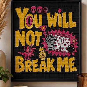 May include: A black framed cross-stitch wall art piece featuring the yellow text "YOU WILL NOT BREAK ME" on a black background. The design includes three pink skulls, a pink dinosaur, a yellow pineapple, a silver gauntlet, and heart-patterned shorts.