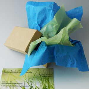 May include: A brown cardboard box wrapped in blue and green tissue paper. The box is labeled "Evolve Jewelry Studio" and includes contact information. The text "keeping wild places close to our heart" is also visible on the box.
