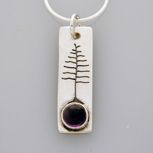 May include: A silver pendant necklace with a rectangular charm featuring a stylized tree design and a purple amethyst gemstone.