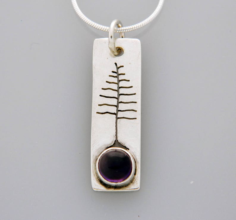 May include: A silver pendant necklace with a rectangular charm featuring a stylized tree design and a purple amethyst gemstone.