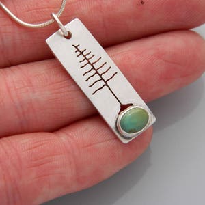 May include: A silver pendant necklace with a cutout tree design and a turquoise stone at the bottom.