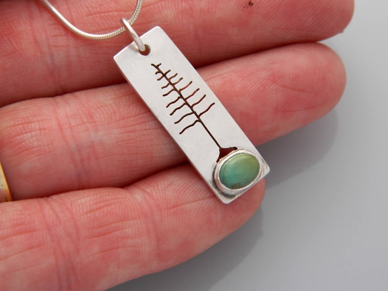 May include: A silver pendant necklace with a cutout tree design and a turquoise stone at the bottom.
