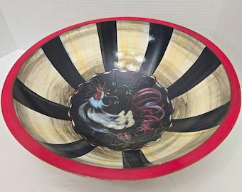 Puede incluir: Un cuenco redondo para servir con un gallo pintado a mano en el centro sobre un fondo negro. Los lados interiores muestran rayas alternas negras y color crema, mientras que el borde exterior tiene un acabado con un borde rojo sólido.