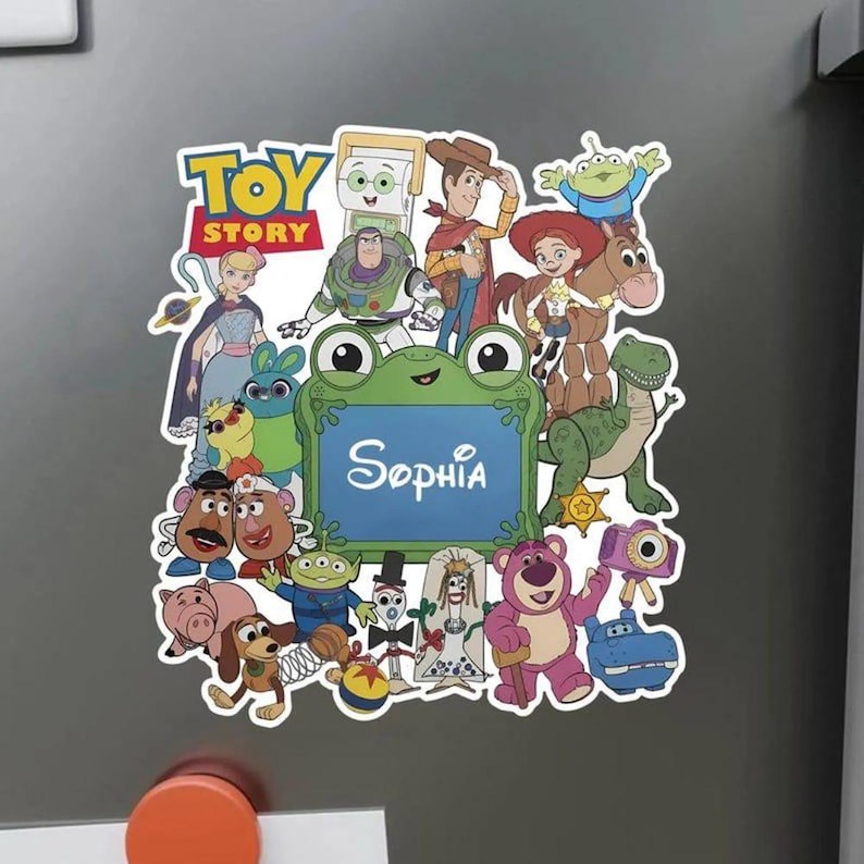 Puede incluir: Un im&aacute;n decorativo con un collage de personajes de Toy Story que rodean un marco central verde con forma de rana y el nombre Sophia impreso en letra cursiva blanca. Los personajes incluyen a Woody, Buzz Lightyear, Jessie y Bullseye.