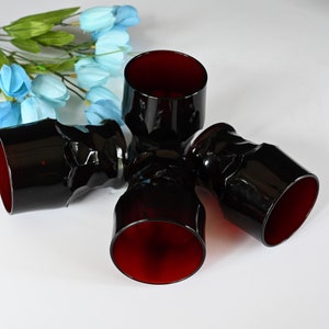 May include: Set of four dark red glass tumblers with a textured design. The glasses are stacked on top of each other.