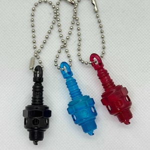 以下が含まれることがあります： 黒、青、赤の3色のスパークプラグキーホルダー。各キーホルダーには、シルバーのボールチェーンと留め金が付いています。プラスチック製のスパークプラグは、詳細なデザインです。キーホルダーはミニチュアのスパークプラグのように見えるように設計されています。
