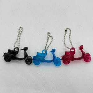 以下が含まれることがあります： 黒、青、赤のミニチュアスクーターキーホルダー3個セット。各スクーターには、取り付け用のシルバーボールチェーンが付いています。スクーターは半透明のプラスチック素材で作られており、クラシックなヴィンテージスタイルです。