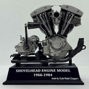 May include: A detailed V-twin Shovelhead engine model mounted on a black rectangular base. The base features the white text SHOVELHEAD ENGINE MODEL 1966-1984 made by Scale Model Choppers. The engine is silver and grey with black accents.
