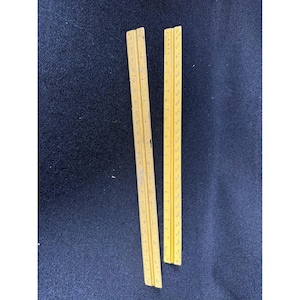 May include: Two vintage wooden rulers with inch and centimeter markings. The rulers are a light yellow color and are lying on a dark blue surface. The rulers are straight and have clear markings.