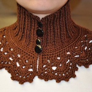 May include: A brown crocheted collar with a lacy edge and three black buttons. The collar is worn by a person, but the person is not visible in the image.