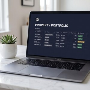 Puede incluir: Un ordenador port&aacute;til MacBook Pro plateado que muestra un "Property Portfolio" en su pantalla. La pantalla muestra una tabla con detalles de la propiedad, incluyendo direcci&oacute;n, tipo, precio y estado. Una peque&ntilde;a planta suculenta en una maceta blanca est&aacute; a la izquierda.