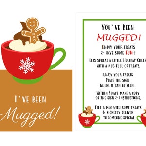 以下が含まれることがあります： 緑色の取っ手と雪の結晶のデザインが施された赤いマグカップ。ジンジャーブレッドマンがホイップクリームとチョコレートソースを添えてマグカップの上に座っています。マグカップの下には「I've Been Mugged!」という文字が書かれています。