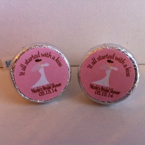 May include: Two silver foil-wrapped chocolate kisses with pink labels. The labels feature a bride in a white dress and the text "It all started with a kiss" and "Nicole's Bridal Shower 05.15.14".