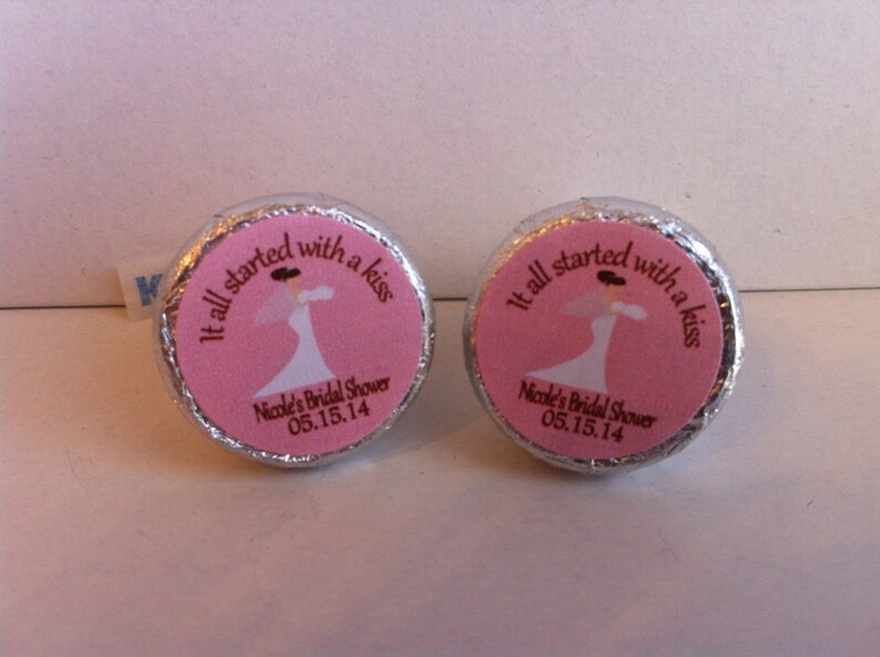 May include: Two silver foil-wrapped chocolate kisses with pink labels. The labels feature a bride in a white dress and the text "It all started with a kiss" and "Nicole's Bridal Shower 05.15.14".