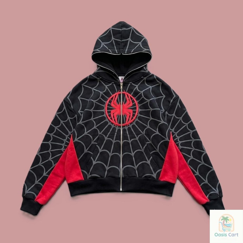 May include: A black zip-up hoodie featuring a grey spiderweb pattern across the front, back, and sleeves. A large red spider emblem is centered on the chest. The garment includes red side panels, a hood, and a full-length silver metal zipper.