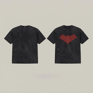 Peut inclure: Un t-shirt à manches courtes et col rond en tissu noir délavé. L'avant présente un grand emblème en forme de chauve-souris rouge vieilli centré sur la poitrine, tandis que le dos est uni, affichant la même texture sombre et mouchetée.