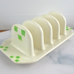 Puede incluir: Tostador de cerámica color crema con cinco ranuras arqueadas. El soporte tiene una base rectangular y está decorado con detalles en forma de diamante verde. Un accesorio de cocina vintage.