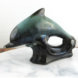 May include: A blue and green glazed ceramic dolphin figurine. The dolphin is leaping out of the water and has a black base.