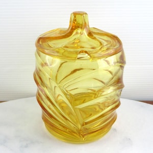 Könnte beinhalten: Eine gelbe Glasdose mit Deckel, die ein wirbelndes, strukturiertes Design aufweist. Die Dose ist perfekt zum Aufbewahren von Zucker, Süßigkeiten oder anderen kleinen Gegenständen.