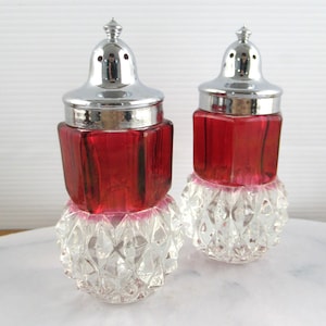 Puede incluir: Un juego de dos saleros y pimenteros vintage. Los saleros están hechos de vidrio transparente con un patrón de diamante texturizado. La parte superior de cada salero es de vidrio rojo con una tapa de metal plateado.