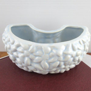 May include: A light blue ceramic planter shaped like a crescent moon with a raised floral design.