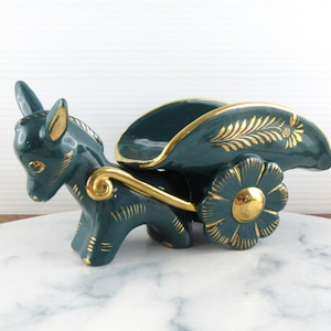 May include: A ceramic donkey-pulled cart figurine in teal with gold accents. The cart features a floral wheel and decorative gold leaf patterns. The donkey has detailed features and is pulling a curved cart.